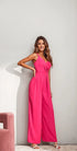 Woman wearing a bright pink Lalita Jumpsuit with spaghetti straps and sweetheart neckline, standing against a white wall.
